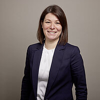 Frau lächelt und trägt einen dunkelblauen Blazer.