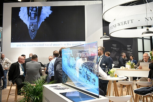 A glass pane with a "hologram" of a ship. A group of men in suits sitting in the background.